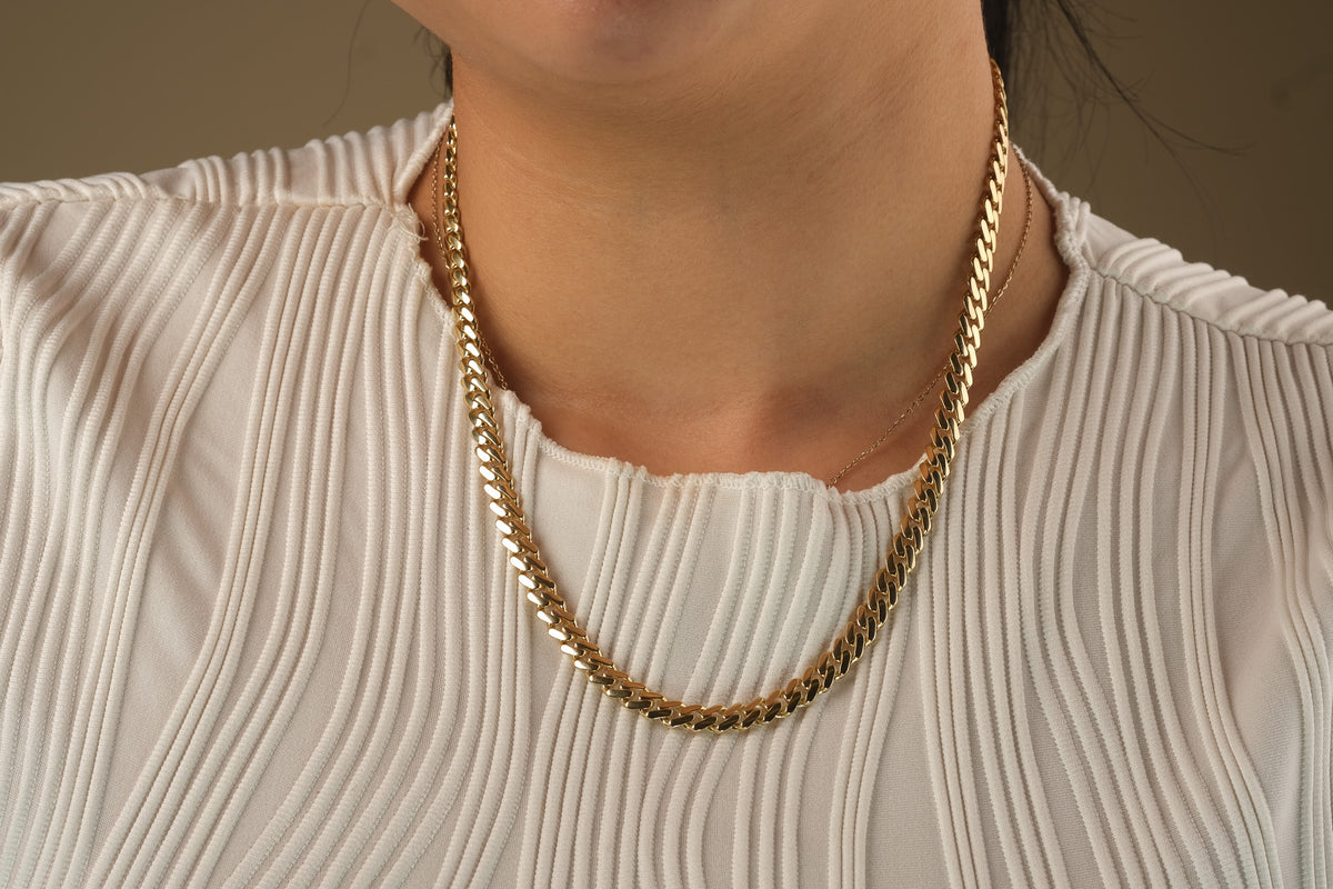 Gold chain necklace worn by a person with a neutral background